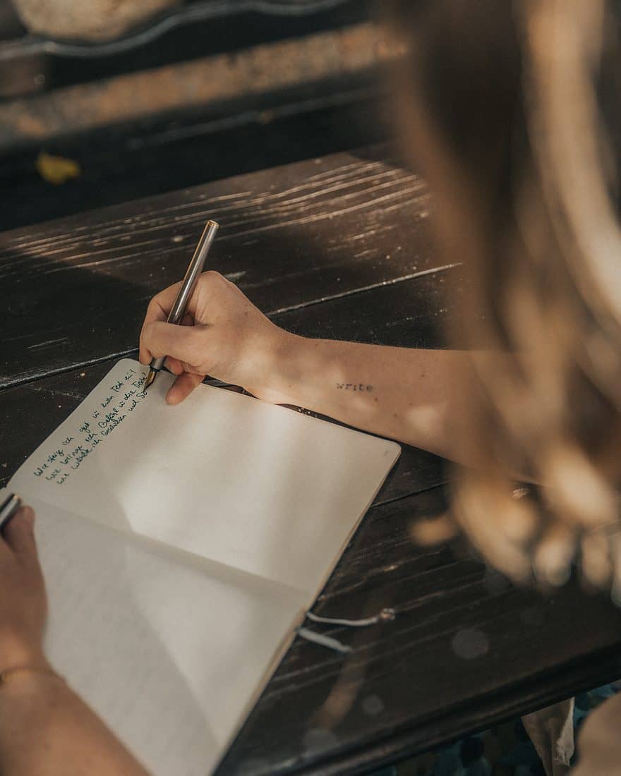 Nahaufnahme: Bianca Fritz schreibt mit Füller in ein Notizbuch, am Unterarm das Tattoo write